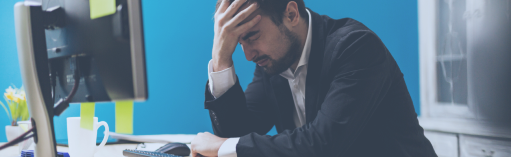 Profissional sentado à secretária com a mão na cabeça, demonstrando stress e receio de denunciar situações problemáticas no ambiente de trabalho